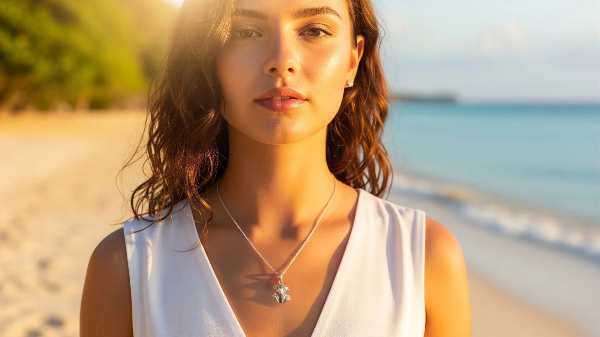 mujer joven iluminada por el sol mientas luce un collar en plata de un coquí, de fondo una hermosa playa de puerto rico